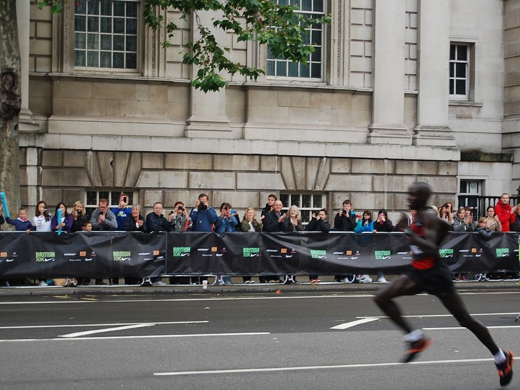 Crowed gathered behind barriers at the finish line. Barrier wraps produced by Colouration